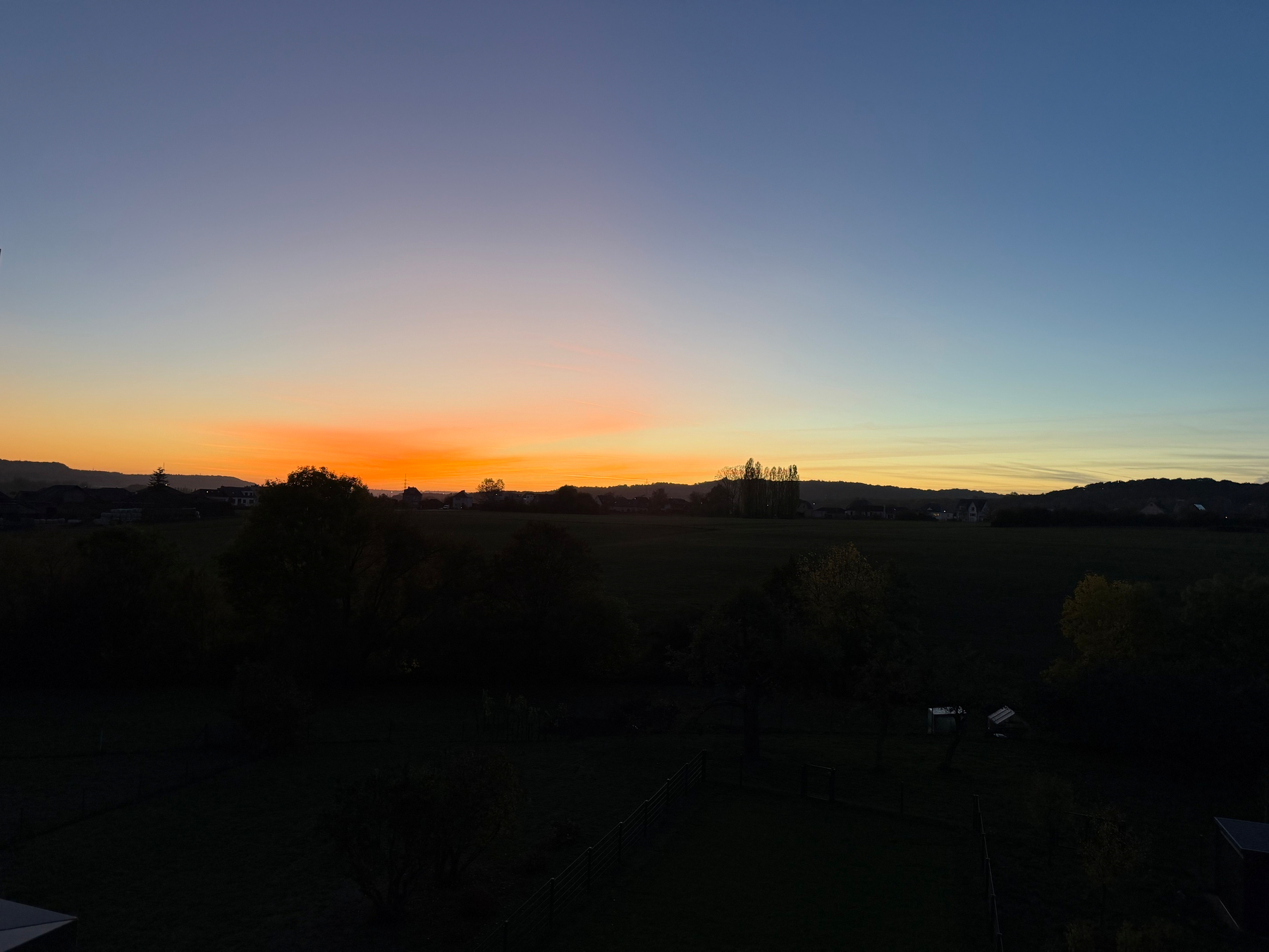 Orange-bloen Owendhimmel iwwer Hautcharage mat Beem a Hiwwelen